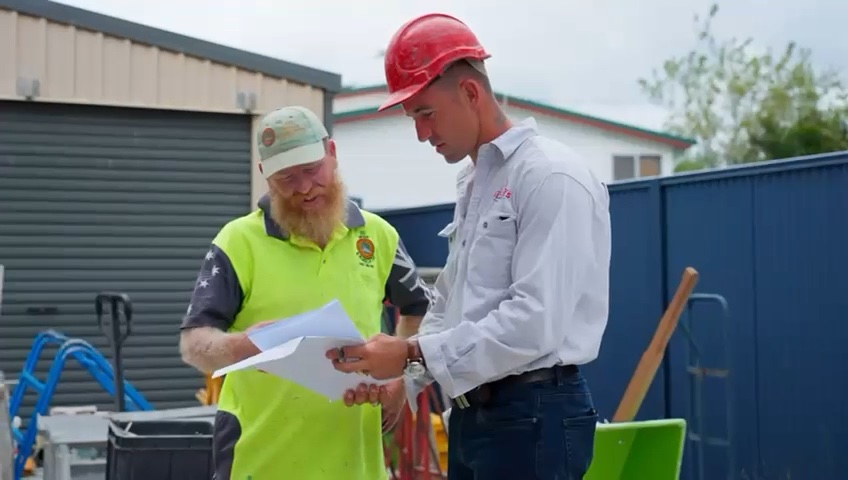 A trainer assessor reviewing paperwork with a tradesperson on site